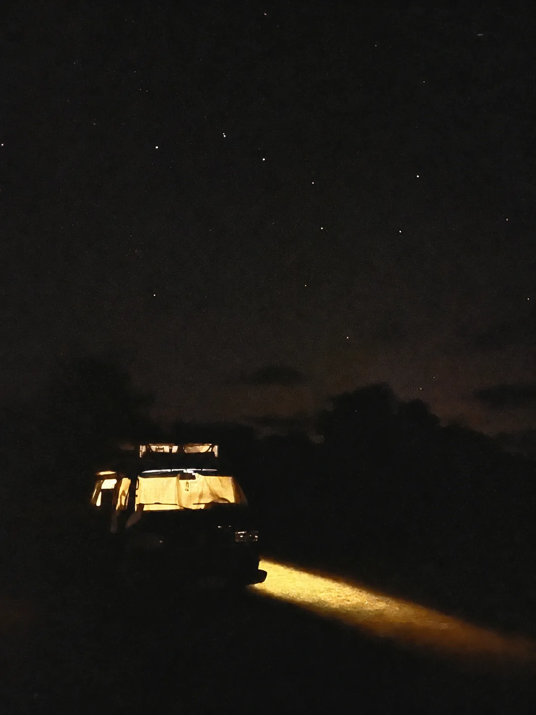 A warm, lit campervan beneath a dark starry sky